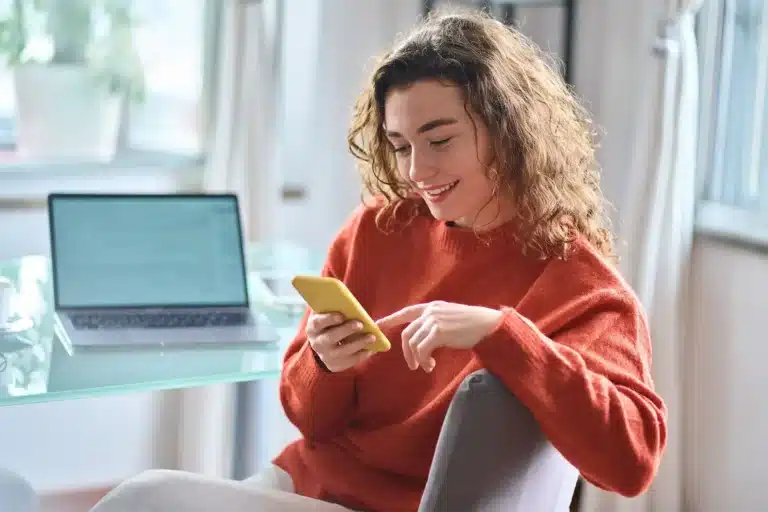 PassportCard/Internationale Krankenversicherung/woman-with-smartphone-sitting-in-front-of-laptop-smiling